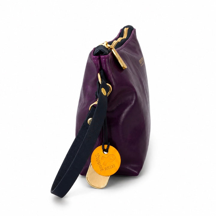 A purple leather bag with gold-tone hardware, a black fabric wristlet strap, and a round gold hangtag, shown on a white background.