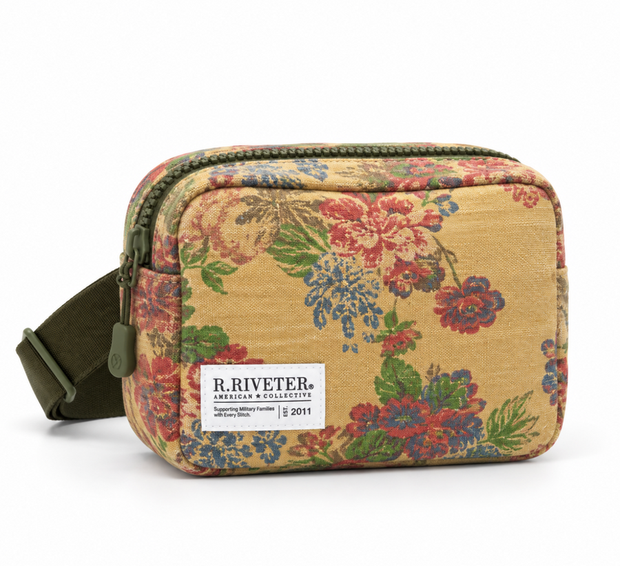 A R. Riveter bag featuring a beige base with a vibrant red, blue, and green floral pattern, complete with an olive green adjustable strap and a white brand label.