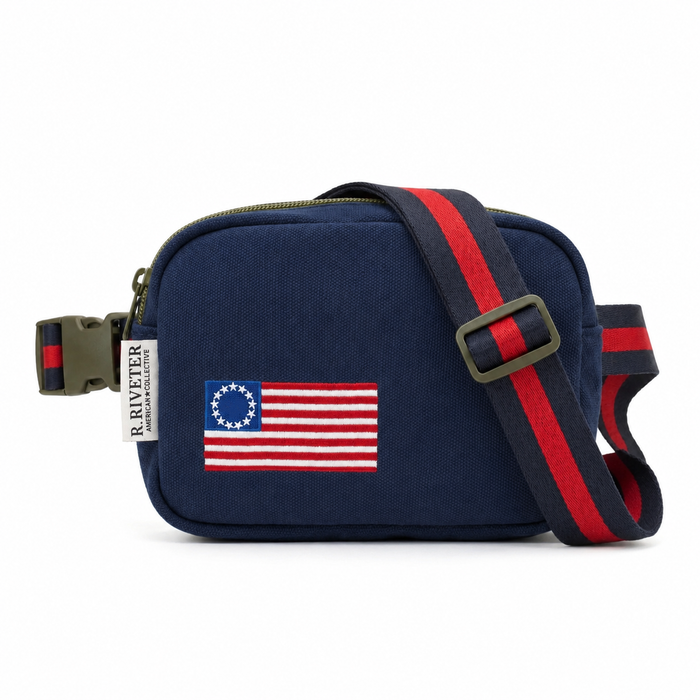 A navy blue canvas crossbody bag with a red and navy striped webbing strap, featuring a Betsy Ross American flag patch on the front and a brand tag that reads 'A.R.