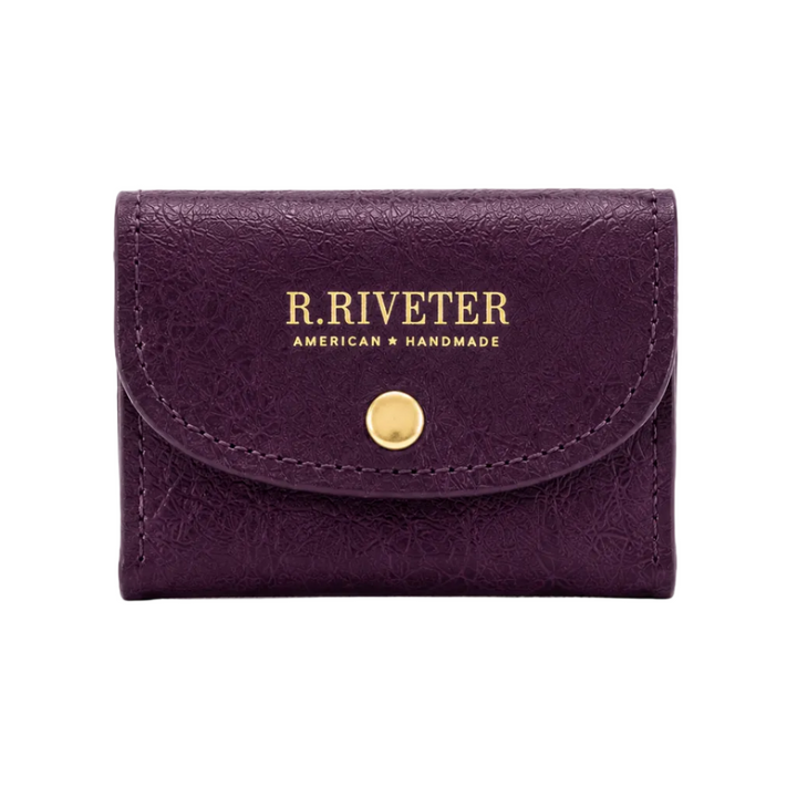 A small purple leather card holder wallet by R. Riveter, featuring gold lettering and a gold snap button closure, set against a plain white background.