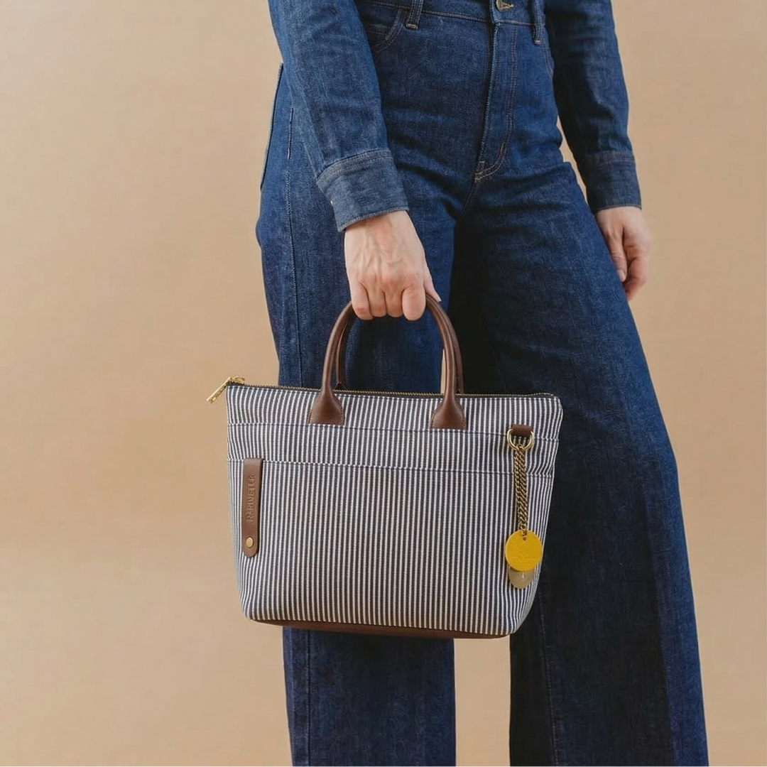 Person wearing a denim outfit holding a striped handbag against a beige background