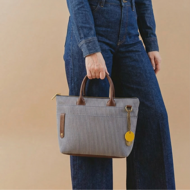 Person wearing a denim outfit holding a striped handbag against a beige background