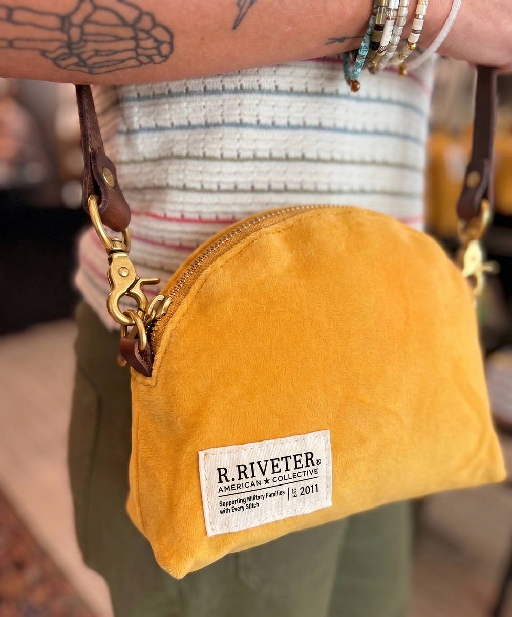 Yellow canvas pouch with 'R. Riveter' label held by a person wearing a striped shirt.