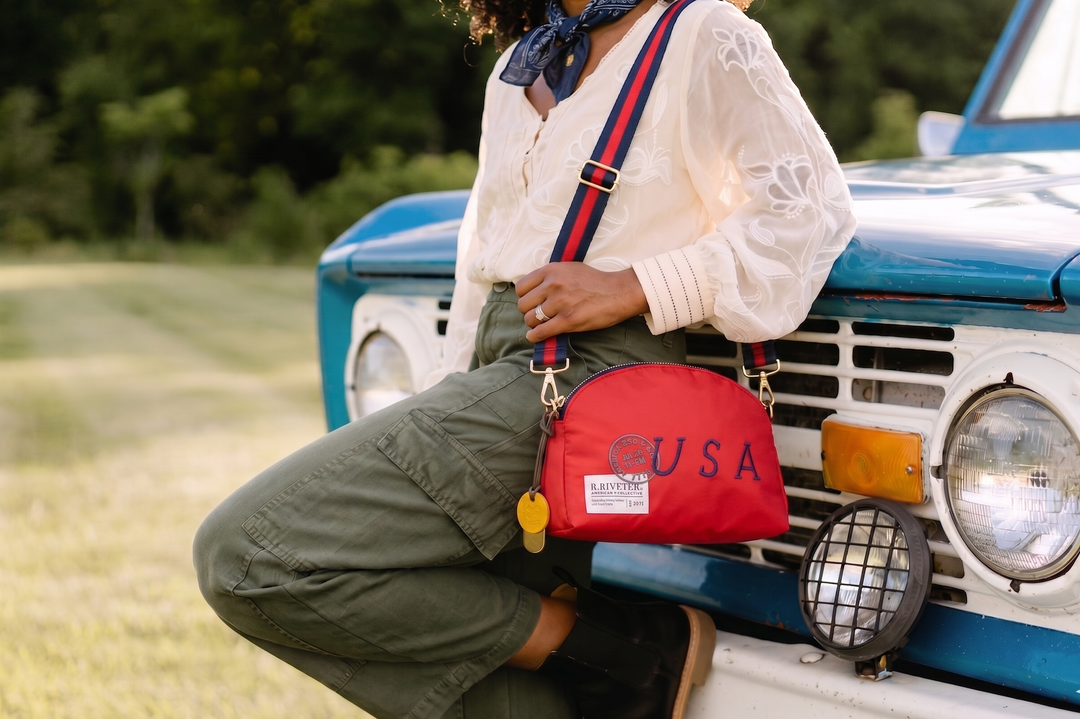 Person with a red bag featuring 'USA' text, leaning against a vintage blue and white truck.