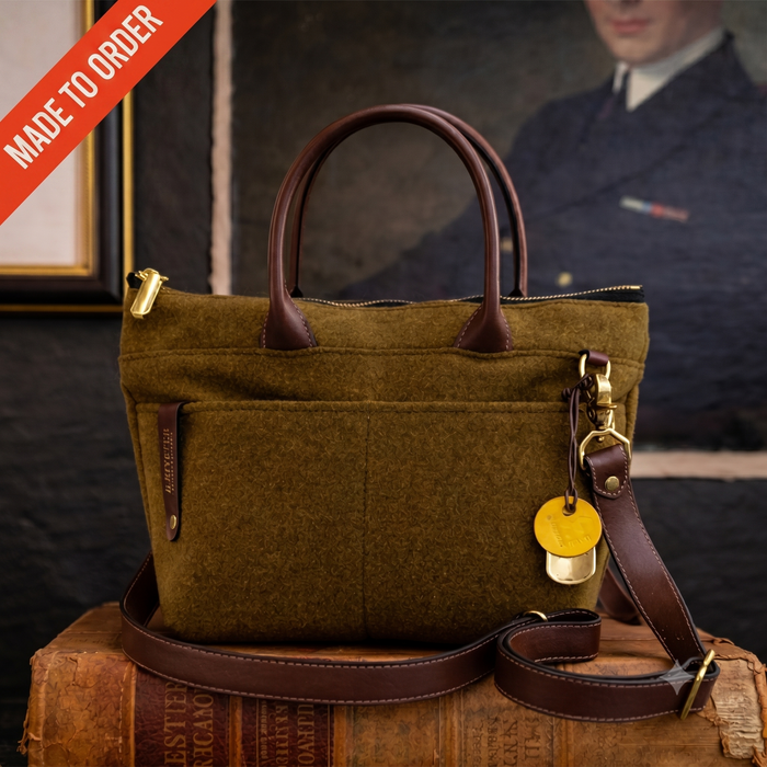 Brown wool handbag with leather straps on a wooden surface, with a blurred background