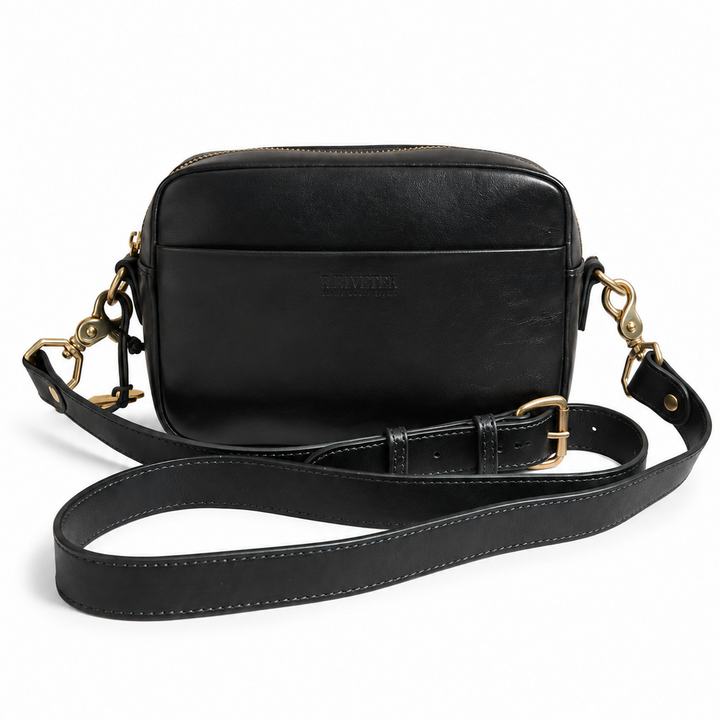 A black leather crossbody camera bag with gold-tone hardware and a detachable shoulder strap, shown on a plain white background.