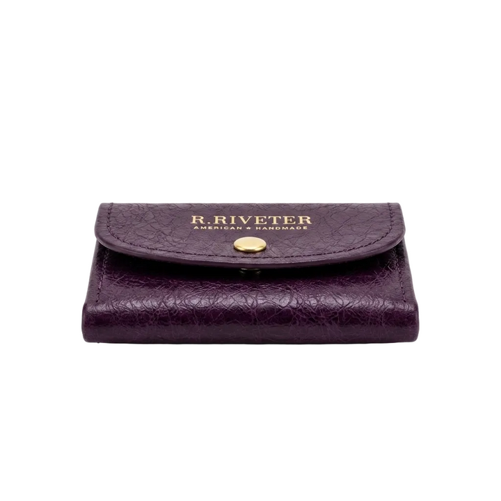 A dark purple textured leather wallet with a gold-tone snap button and gold embossed 'R. RIVETER' branding on the front flap, set against a plain white background.