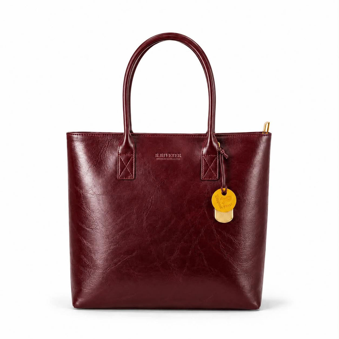 A burgundy faux-leather tote bag with dual top handles, a gold-tone zipper, and a hanging gold tag, shown on a plain white background.