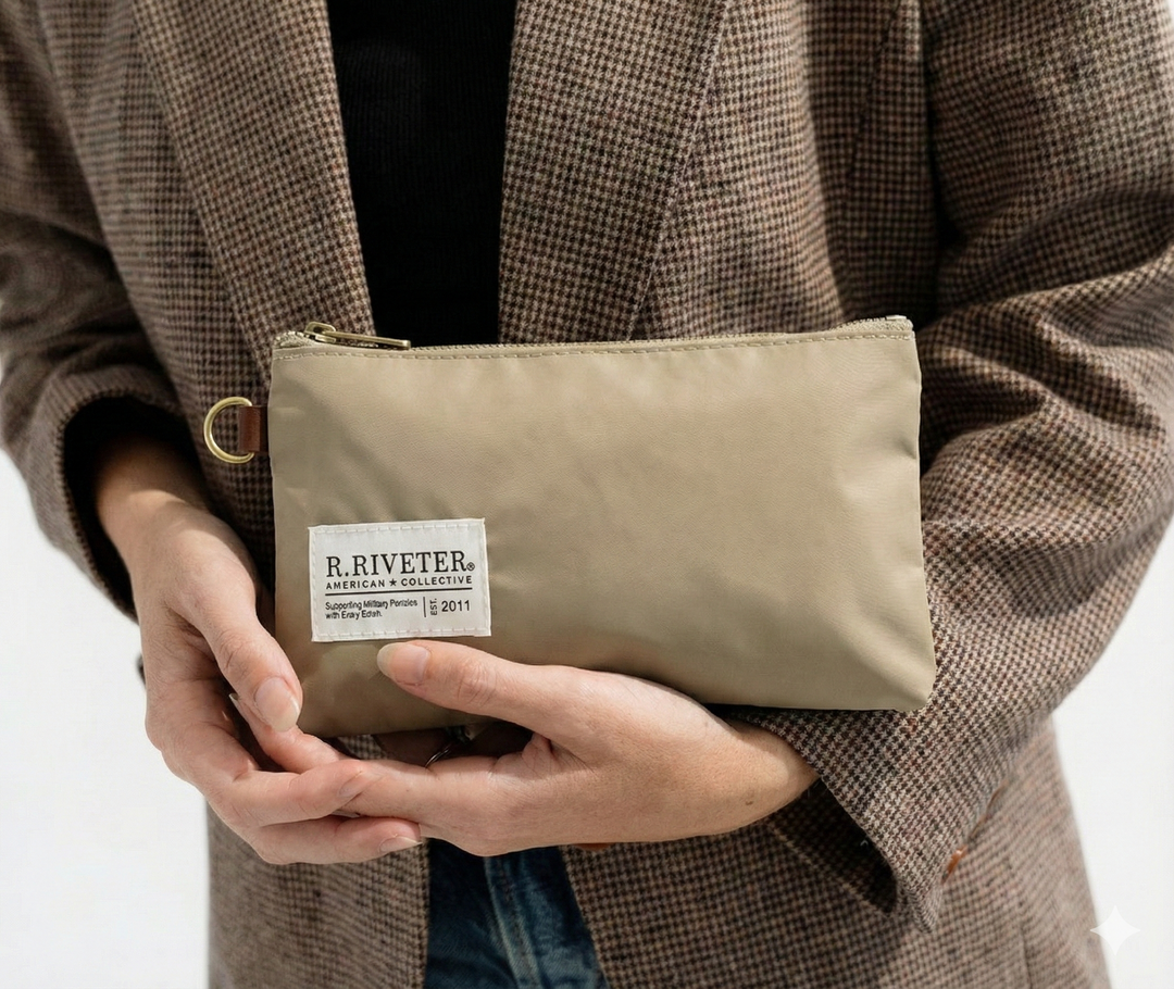 Person holding a beige pouch with a visible brand label against a neutral background