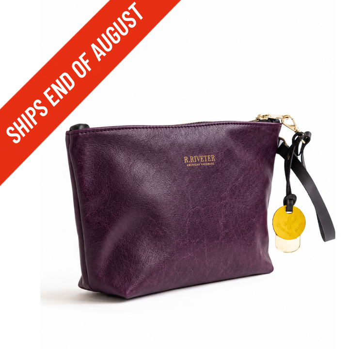 A purple leather wristlet clutch bag with a black wrist strap and gold-tone hardware, featuring the 'R. Riveter' logo.