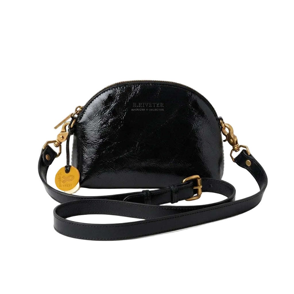 A black patent leather crescent-shaped crossbody bag by Kleveteer, featuring gold-tone hardware, a detachable black strap, and a small gold tag, set against a plain white background.