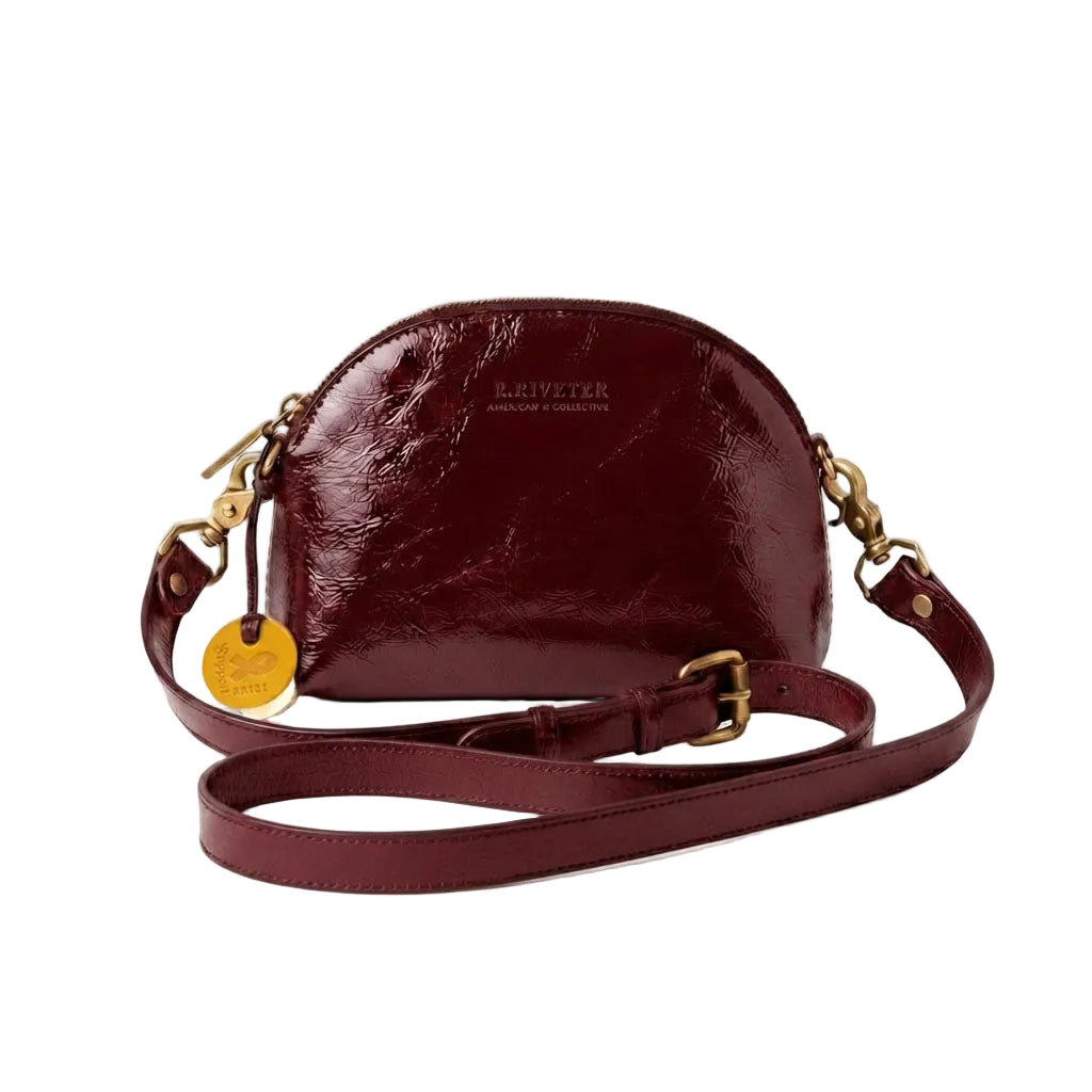 A burgundy crescent-shaped leather shoulder bag with a glossy finish, gold-tone hardware, and a matching adjustable shoulder strap, shown on a plain white background.