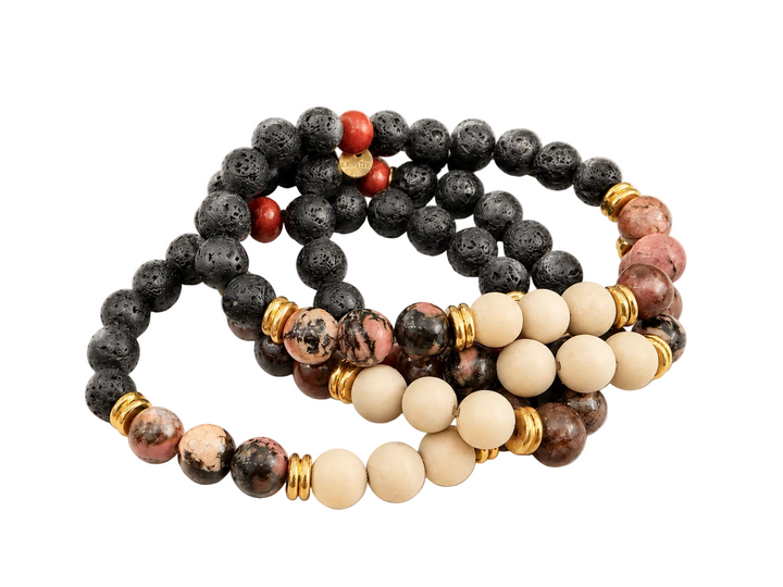 A multi-strand beaded necklace featuring black lava stones, cream-colored wooden beads, pinkish-brown jasper, and small red accent beads separated by gold spacers, displayed on a clean white background.
