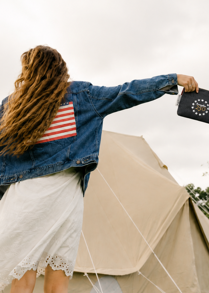 Woman standing in front of a tent with an American flag on her denim jacket, holding a black bag.