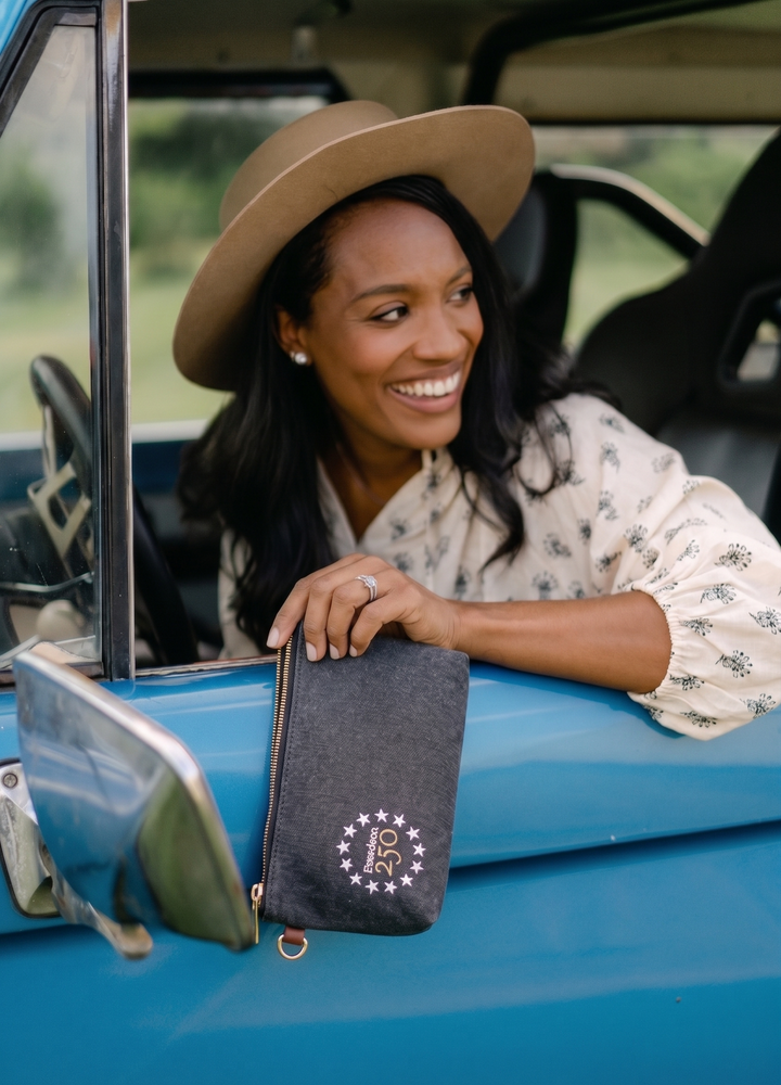 Woman in a car holding a blue bag with a logo, wearing a beige hat.